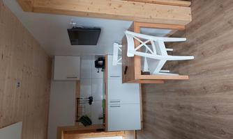 A modern kitchenette with a small dining table and a chair. The room has bright walls and a spacious, welcoming character.