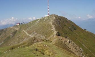 A steep mountain slope with a transmission station at the top. The surroundings are green and the sky is clear.