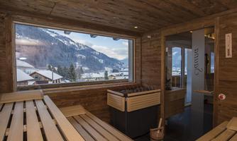 A cozy wellness area with a wood sauna and a view of snow-covered mountains. The atmosphere is relaxing and inviting.