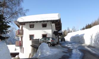 A snow-covered house on a mountain path. The sky is clear and blue.