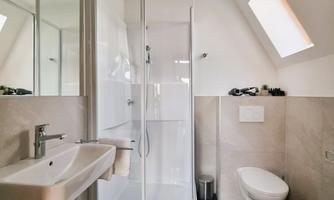 A modern bathroom with a shower cubicle and a sink. The walls are light and the floor is tiled in dark colors.