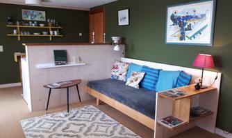 A modern living room with a cozy sofa, colorful cushions, and a small table. The walls are painted in a calming shade of green, and there is an appealing art decoration.