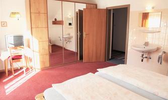 A simple room with two beds, a table, and a television. The room has a large mirror and an en-suite bathroom.