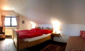 A cozy bedroom with a large double bed and red blankets. There is an armchair and a windowsill that provide plenty of light.