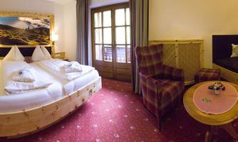 A cozy hotel room with a large bed and a beautiful view of nature. There is an armchair and a small table that create an inviting atmosphere.
