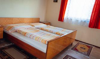A simple bedroom with a wooden bed and striped bedcovers. Red curtains let the light in.
