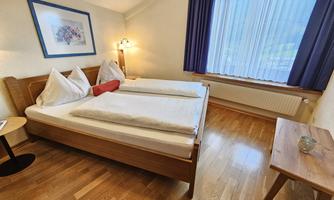 A cozy bedroom with two beds and wooden paneling. Large windows let in plenty of light and create an inviting atmosphere.