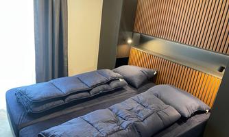 A modern bedroom with two single beds and cozy duvets. The wood paneling and curtains give the room a warm atmosphere.