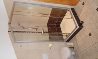 A modern bathroom with a glass shower and a toilet. The walls are bright and the floor has a light tile surface.