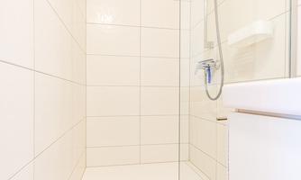 A modern shower with white tiles and a clear glass partition. The room is bright and clean.