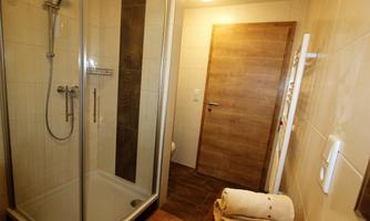 A modern bathroom with a shower and a wooden door. The walls are brightly tiled and towels are ready.