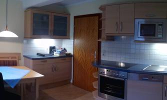 A modern kitchen with wooden cabinets and bright furniture. There is a dining table and various kitchen appliances.