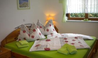 A cozy bedroom with a large bed and colorful pillows. The room has bright curtains and is well lit.