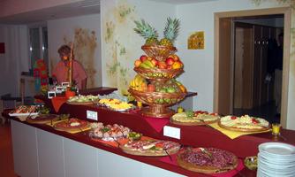 A lavish buffet with various foods, including fruit, meat, and cake. In the background, there is a person managing the buffet.