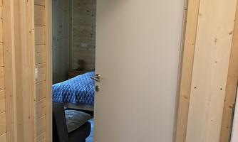 An open door to a room with wooden walls. In the background, there is a bed with blue bedding.