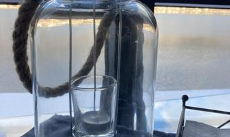 A large glass lantern with a rope handle and a small glass inside. It sits on a table and looks elegant and modern.