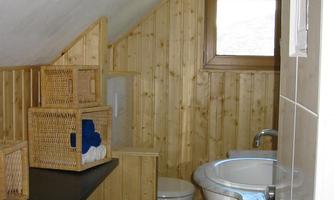 A small bathroom with wooden paneling and a sloped roof. There is a sink, a toilet, and storage baskets.