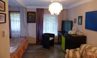 Double bed, seating area with glass table, desk with TV and tea station, window with curtains and a blue infrared panel on the wall.