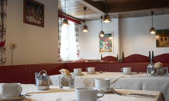 A cozy restaurant with tables set for guests. The walls are decorated and there is charming lighting.