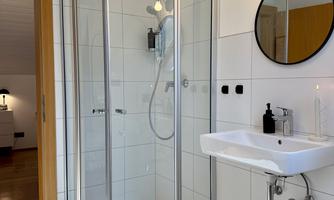 A modern bathroom with a glass shower and an elegant sink. The walls are designed with white tiles, and there is a large round mirror.