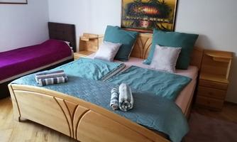 A cozy bedroom with a large wooden bed and bright pillows. Another mattress is next to it, and fresh towels are draped on the bed.