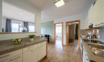 A modern kitchen with bright cabinets and wooden flooring. The space is well-lit and offers an open view of the living room.