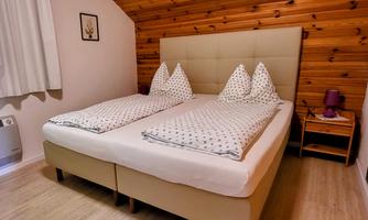 A cozy bedroom with a double bed and wooden ceilings. The bedding is neatly arranged, and a bedside table stands beside it.