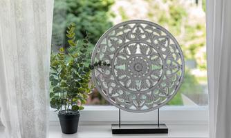 A decorative wall panel with a delicate pattern is placed on the windowsill. Next to it is a small pot with a green plant.