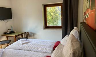 A cozy hotel room with two beds and a window overlooking a green outdoor area. There is a TV and a small table.