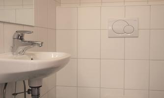 A small bathroom with a sink and a toilet. The walls are tiled with white tiles.