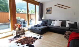 A cozy living room with a gray sofa and large windows that let in plenty of daylight. The room features a cowhide blanket and some decorative items.