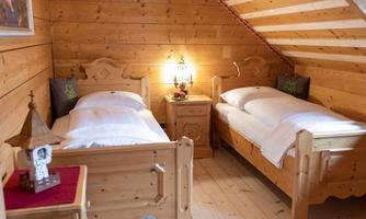A cozy bedroom with two wooden single beds. The walls are paneled with wood and there is a warm lamp on the bedside table.
