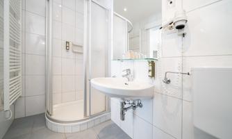 A modern bathroom with a shower cabin and a sink. The walls are white and the floor is tiled.