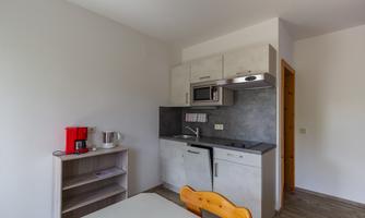 A modern kitchen with bright cabinets and a kitchen table. The equipment includes a microwave, a kettle, and a refrigerator.