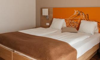 A modern bedroom with a double bed and colorful wall decoration. The floor is made of wood and the walls are kept neutral.