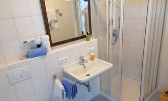 A modern bathroom with sink, mirror, and shower. The walls are brightly tiled and decorated with towels.