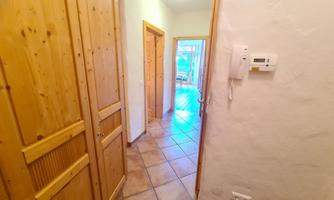 A bright hallway with wooden cabinets and tiled flooring. In the background, there are windows letting in natural light.
