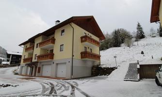 A modern building with several floors in a snow-covered landscape. In the background, there are spruce trees and a cloudy sky.