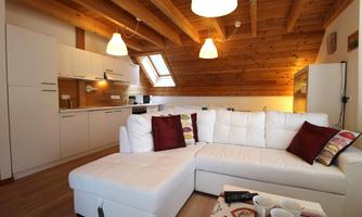 A modern living room with a white couch and wooden ceiling. The open kitchen is well-equipped and invites relaxation.