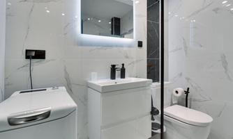 A modern bathroom with white tiles and elegant fixtures. It features a sink, a toilet, and a shower.