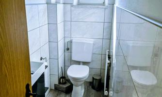 A modern bathroom with WC and a small window. The walls are tiled with white tiles and the floor is made of wood.