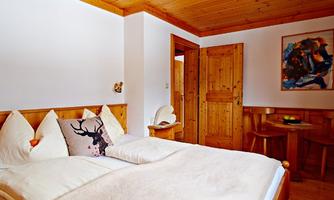 A cozy bedroom with wooden paneling and a large bed. The room has a warm atmosphere and a small seating area.