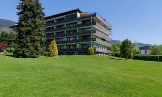 A modern building surrounded by green grass and trees. The sunny landscape conveys a calm and pleasant atmosphere.