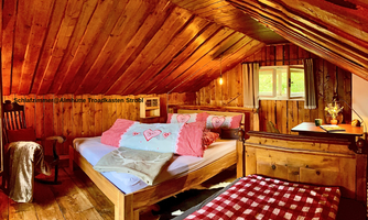 A cozy bedroom in the attic with wood paneling. It contains a bed with colorful pillows and a small table next to a window.