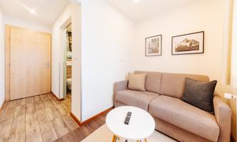 A modern living room with a gray sofa and a small table. Framed pictures hang on the wall, and the room has a bright, inviting feel.