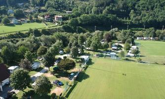A green space with a soccer field and several camping sites. Surrounded by trees and hills, the landscape offers a tranquil natural atmosphere.