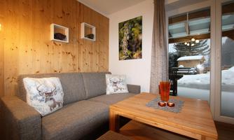 A cozy living room with a gray sofa and a wooden table. Through the windows, you can see snow and a serene winter landscape.