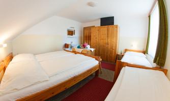 A cozy room with three beds, a wardrobe, and a small table. The walls are bright, and the room has a friendly atmosphere.