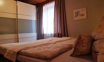 A cozy bedroom with a large bed and a wardrobe. The window lets in gentle light and creates an inviting atmosphere.