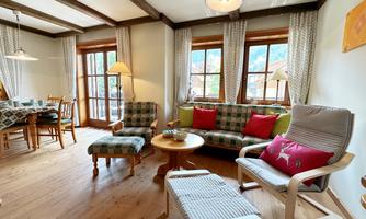 A cozy living space with wooden floors and large windows. The room is furnished with a sofa, armchairs, and a table, creating an inviting atmosphere.